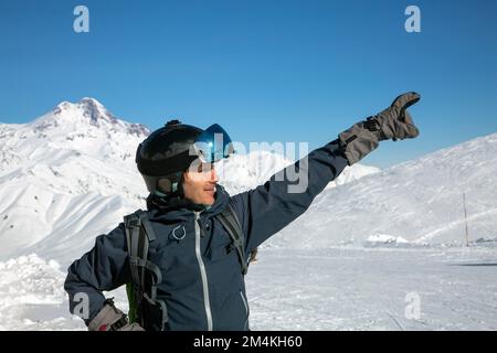 Der Kopfschuss eines fröhlichen Skifahrers zeigt die Richtung nach oben und trägt einen Skihelm und eine Schutzbrille. Gudauri, Kaukasus, Georgien Stockfoto