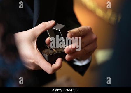 Ein oberflächliches Fokusfoto von Männerhänden, die Eheringe in einer Blackbox halten Stockfoto