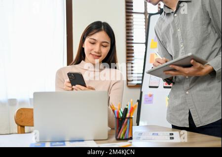 Professionelle Millenials asiatischer Entwickler, die mit ihrem Kollegen an einem neuen Prototyp für mobile Anwendungen arbeiten. UI UX-Konzept für Unternehmensgründungen Stockfoto