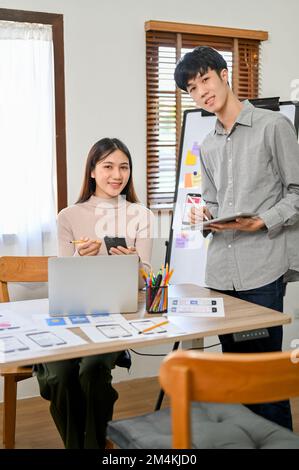 Attraktive und professionelle Entwickler der Millennials in Asien sind im Konferenzraum, lächeln und schauen in die Kamera. Stockfoto