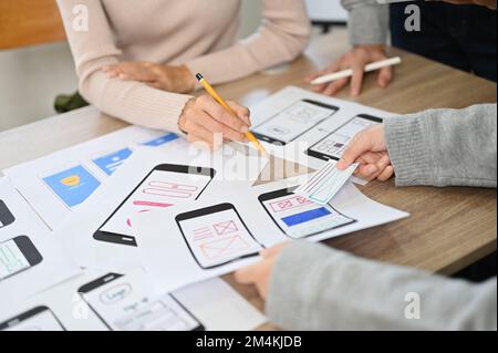 Ein Team von Entwicklern und Designern mobiler Apps diskutiert und führt ein Brainstorming zu ihrem neuen Design für die Benutzeroberfläche mobiler Apps durch. Zugeschnittenes Bild Stockfoto