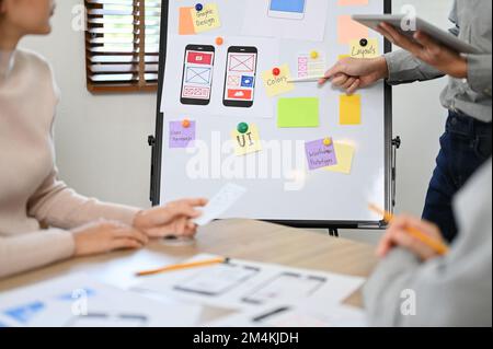 Professioneller junger, männlicher asiatischer Softwareentwickler, der seinen Kollegen während des Meetings seine Informationen für eine neue mobile Anwendung vorstellt. UI-UX-Busin Stockfoto