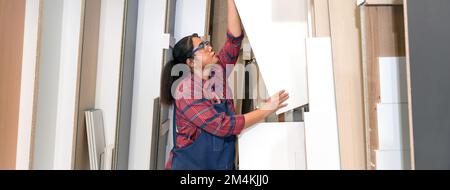 Eine Frau mittleren Alters, die Sperrholz aus einem Lagerfach zieht. Asiatischer Zimmermann arbeitet in einer Möbelfabrik. Stockfoto