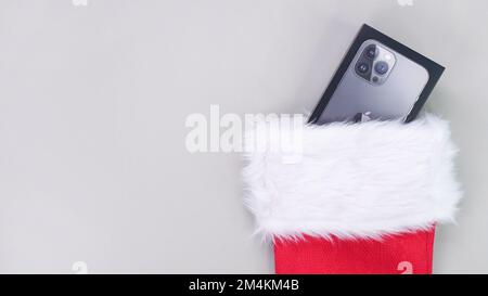 Die iPhone-Geschenkbox sieht aus wie Weihnachtssocken. Der rote Strumpf des Weihnachtsmanns ist voller Geschenke. Konzept von weihnachten oder Feiertagen. Geschenke auf grauem Hintergrund. Gatinea Stockfoto