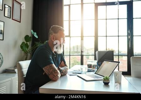 HES speziell für Design. Ein gut aussehender, reifer Geschäftsmann, der im Büro an seinem Laptop arbeitet. Stockfoto