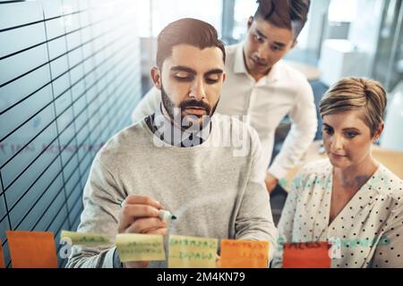 Was wäre, wenn wir Ideen kombinieren? Brainstorming von Geschäftsleuten mit Haftnotizen an einer Glaswand im Büro. Stockfoto