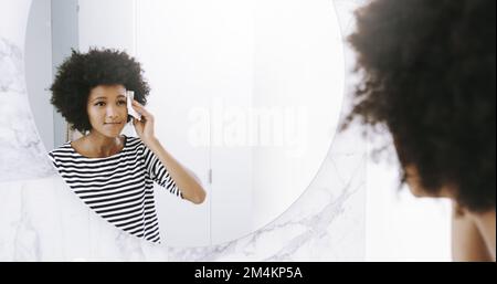 Ich werde sauber und sauber. Eine selbstbewusste junge Frau wischte sich mit einem Reinigungsmittel ins Gesicht, während sie tagsüber in einen Spiegel im Badezimmer schaute. Stockfoto