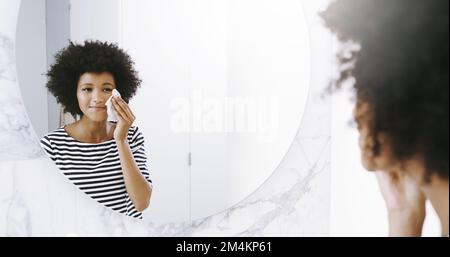 Sie sieht jeden Tag perfekt aus. Eine selbstbewusste junge Frau wischte sich das Gesicht mit einem Reinigungsmittel, während sie zu Hause in einen Spiegel im Badezimmer schaute Stockfoto