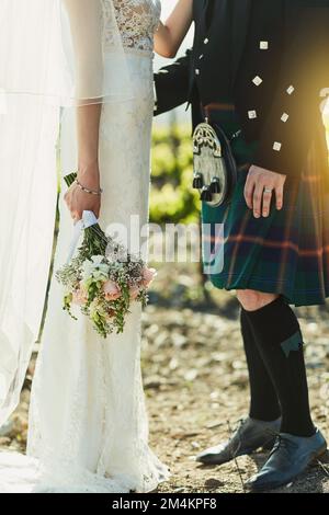 Wie traditionell. Eine nicht wiedererkennbare Braut und ein Bräutigam halten sich gegenseitig, während sie tagsüber neben den Weinbergen stehen. Stockfoto