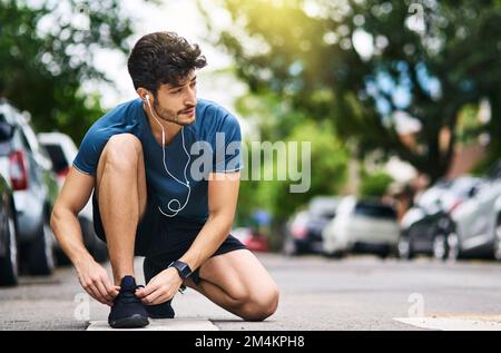 Das beste Projekt, an dem du je gearbeitet hast, bist du. Ein sportlicher junger Mann, der seine Schnürsenkel bindet, während er draußen trainiert. Stockfoto