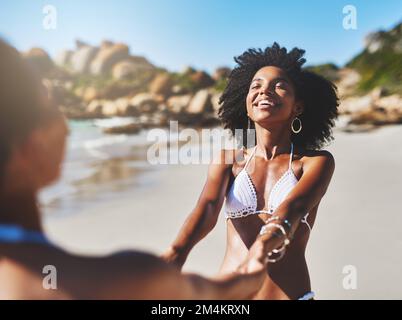 Gute Zeiten machen die Welt zum Laufen. Zwei junge Frauen genießen einen verspielten Moment am Strand. Stockfoto