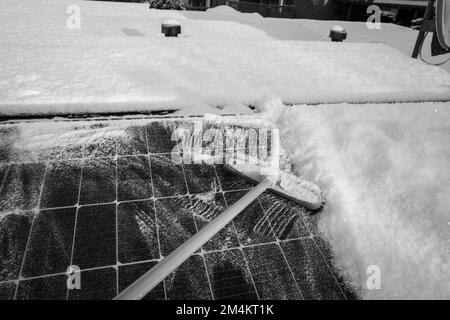 Die Sonnenkollektoren auf dem Dach werden mit einem Besen von Schnee gereinigt Stockfoto