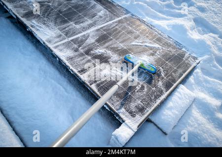 Die Sonnenkollektoren auf dem Dach werden mit einem Besen von Schnee gereinigt Stockfoto