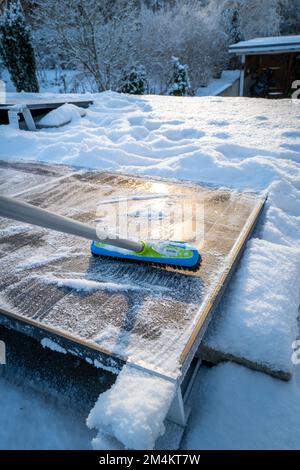 Die Sonnenkollektoren auf dem Dach werden mit einem Besen von Schnee gereinigt Stockfoto