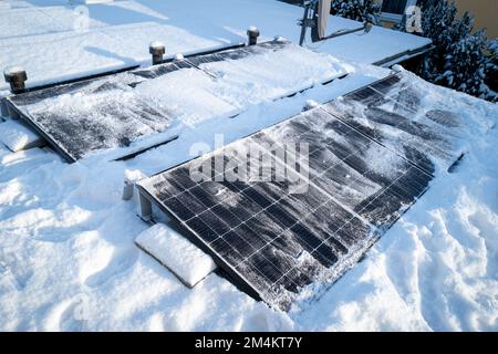 Die Sonnenkollektoren auf dem Dach werden mit einem Besen von Schnee gereinigt Stockfoto