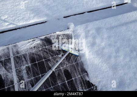 Die Sonnenkollektoren auf dem Dach werden mit einem Besen von Schnee gereinigt Stockfoto