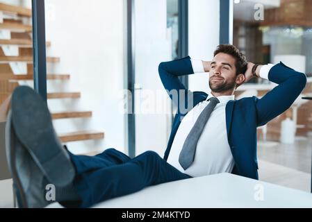 Wenn du in dich selbst investierst und es sich auszahlt. Ein gutaussehender junger Geschäftsmann, der sich mit den Füßen auf dem Schreibtisch in einem modernen Büro entspannt. Stockfoto