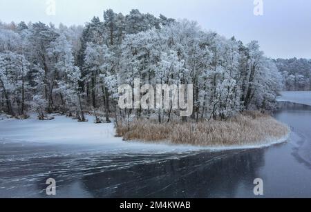 Treplin, Deutschland. 18. Dezember 2022. Ein wenig Schnee liegt in einem Wald an einem See, der teilweise gefroren ist und die Bäume sind mit Heiserfrost bedeckt (Luftaufnahme mit einer Drohne). Kredit: Patrick Pleul/dpa/Alamy Live News Stockfoto