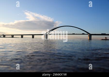 Fehmarn, Deutschland. 16.. Dezember 2022. Die Fahrzeuge fahren über die Fehmarnsund-Brücke unter blauem Himmel. Die Arbeiten an der Baustelle für den geplanten Ostsee-Tunnel in der Nähe von Puttgarden auf der Insel Fehmarn gehen voran. Der 18 km lange Straßen- und Eisenbahntunnel verbindet die Insel Fehmarn mit der dänischen Insel Lolland ab 2029. Laut Femern A/S belaufen sich die Kosten auf 7,1 Milliarden Euro. Kredit: Christian Charisius/dpa/Alamy Live News Stockfoto