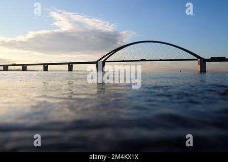 Fehmarn, Deutschland. 16.. Dezember 2022. Die Fahrzeuge fahren über die Fehmarnsund-Brücke unter blauem Himmel. Die Arbeiten an der Baustelle für den geplanten Ostsee-Tunnel in der Nähe von Puttgarden auf der Insel Fehmarn gehen voran. Der 18 km lange Straßen- und Eisenbahntunnel verbindet die Insel Fehmarn mit der dänischen Insel Lolland ab 2029. Laut Femern A/S belaufen sich die Kosten auf 7,1 Milliarden Euro. Kredit: Christian Charisius/dpa/Alamy Live News Stockfoto