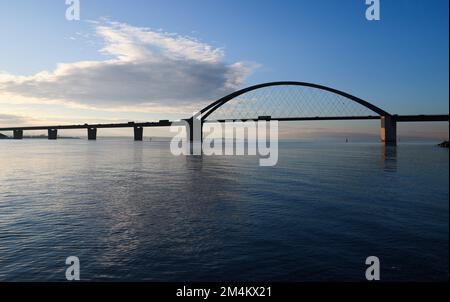 Fehmarn, Deutschland. 16.. Dezember 2022. Die Fahrzeuge fahren über die Fehmarnsund-Brücke unter blauem Himmel. Die Arbeiten an der Baustelle für den geplanten Ostsee-Tunnel in der Nähe von Puttgarden auf der Insel Fehmarn gehen voran. Der 18 km lange Straßen- und Eisenbahntunnel verbindet die Insel Fehmarn mit der dänischen Insel Lolland ab 2029. Laut Femern A/S belaufen sich die Kosten auf 7,1 Milliarden Euro. Kredit: Christian Charisius/dpa/Alamy Live News Stockfoto