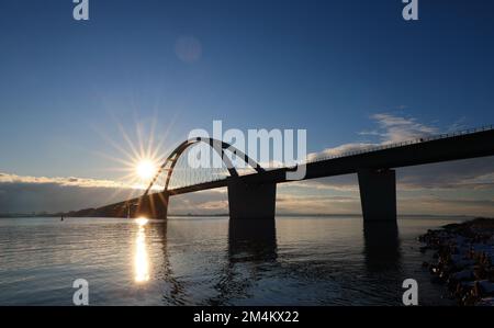 Fehmarn, Deutschland. 16.. Dezember 2022. Die Fahrzeuge fahren über die Fehmarnsund-Brücke unter blauem Himmel. Die Arbeiten an der Baustelle für den geplanten Ostsee-Tunnel in der Nähe von Puttgarden auf der Insel Fehmarn gehen voran. Der 18 km lange Straßen- und Eisenbahntunnel verbindet die Insel Fehmarn mit der dänischen Insel Lolland ab 2029. Laut Femern A/S belaufen sich die Kosten auf 7,1 Milliarden Euro. Kredit: Christian Charisius/dpa/Alamy Live News Stockfoto