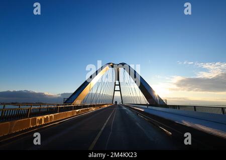 Fehmarn, Deutschland. 16.. Dezember 2022. Die Fahrzeuge fahren über die Fehmarnsund-Brücke unter blauem Himmel. Die Arbeiten an der Baustelle für den geplanten Ostsee-Tunnel in der Nähe von Puttgarden auf der Insel Fehmarn gehen voran. Der 18 km lange Straßen- und Eisenbahntunnel verbindet die Insel Fehmarn mit der dänischen Insel Lolland ab 2029. Laut Femern A/S belaufen sich die Kosten auf 7,1 Milliarden Euro. Kredit: Christian Charisius/dpa/Alamy Live News Stockfoto