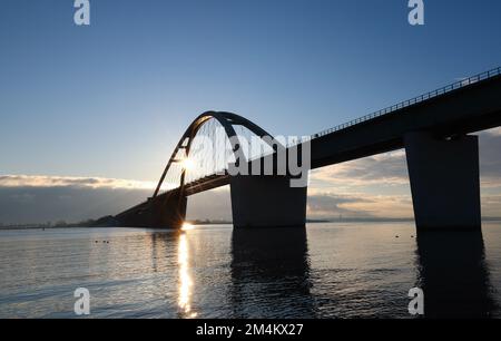 Fehmarn, Deutschland. 16.. Dezember 2022. Die Fahrzeuge fahren über die Fehmarnsund-Brücke unter blauem Himmel. Die Arbeiten an der Baustelle für den geplanten Ostsee-Tunnel in der Nähe von Puttgarden auf der Insel Fehmarn gehen voran. Der 18 km lange Straßen- und Eisenbahntunnel verbindet die Insel Fehmarn mit der dänischen Insel Lolland ab 2029. Laut Femern A/S belaufen sich die Kosten auf 7,1 Milliarden Euro. Kredit: Christian Charisius/dpa/Alamy Live News Stockfoto