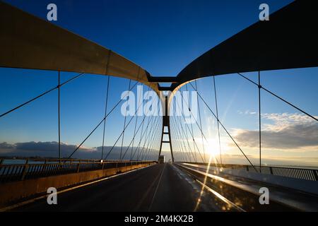 Fehmarn, Deutschland. 16.. Dezember 2022. Die Fahrzeuge fahren über die Fehmarnsund-Brücke unter blauem Himmel. Die Arbeiten an der Baustelle für den geplanten Ostsee-Tunnel in der Nähe von Puttgarden auf der Insel Fehmarn gehen voran. Der 18 km lange Straßen- und Eisenbahntunnel verbindet die Insel Fehmarn mit der dänischen Insel Lolland ab 2029. Laut Femern A/S belaufen sich die Kosten auf 7,1 Milliarden Euro. Kredit: Christian Charisius/dpa/Alamy Live News Stockfoto