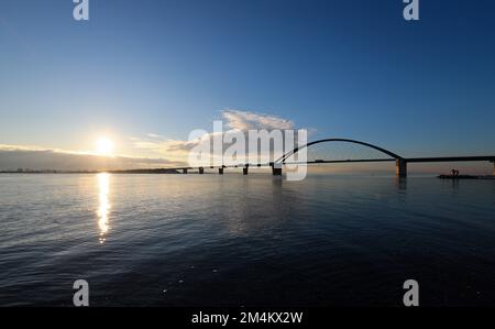 Fehmarn, Deutschland. 16.. Dezember 2022. Die Fahrzeuge fahren über die Fehmarnsund-Brücke unter blauem Himmel. Die Arbeiten an der Baustelle für den geplanten Ostsee-Tunnel in der Nähe von Puttgarden auf der Insel Fehmarn gehen voran. Der 18 km lange Straßen- und Eisenbahntunnel verbindet die Insel Fehmarn mit der dänischen Insel Lolland ab 2029. Laut Femern A/S belaufen sich die Kosten auf 7,1 Milliarden Euro. Kredit: Christian Charisius/dpa/Alamy Live News Stockfoto