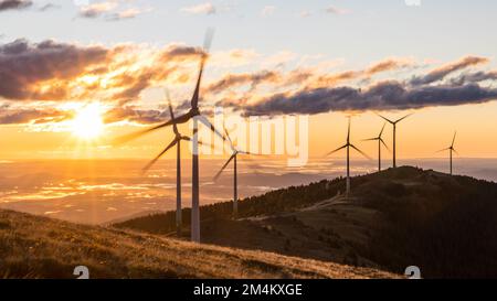 Eine Gruppe von Windmühlen auf einem Bergkamm vor einem Morgenhimmel bei Sonnenaufgang in Österreich Stockfoto