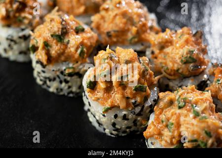 Frische Sushi-Brötchen mit Lachs, Avocado, Muscheln und schwarzen Sesamsamen, serviert auf einem schwarzen Steinschiefer. Japanisches Sushi-Uramaki oder California Roll. Schließen Stockfoto