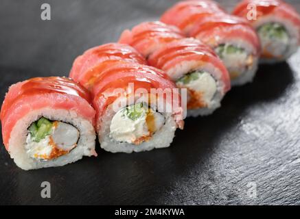 Sushi-Brötchen aus Uroaki mit Garnelentiger, Kaviar und Unagi, bedeckt mit Thunfisch auf schwarzem Hintergrund. Sushi-Menü. Japanische Küche, Restaurant. Stockfoto