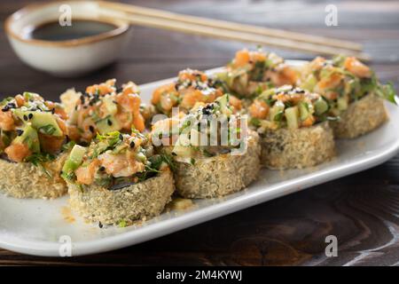 Japanische Tempura-Sushi-Brötchen auf weißem Teller auf Holzhintergrund. Sushi-Stücke mit Lachs, Gurke, Frischkäse, Avocado in knusprigem Nähzeug Stockfoto