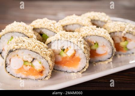 Japanische Tempura-Sushi-Brötchen auf weißem Teller auf Holzhintergrund. Sushi-Stücke mit Lachs, Frischkäse, Avocado in Reis verpackt mit knusprigem Nähen Stockfoto