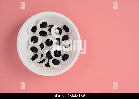 Weiße Schüssel aus Plastik mit schönen Augen auf pinkfarbenem Hintergrund Stockfoto