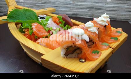 Eine Nahaufnahme von leckerem Sushi, serviert auf einer hölzernen, bootförmigen Platte in einem japanischen Restaurant Stockfoto