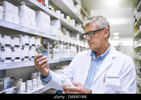 Das hätte nicht hier sein sollen. Ein fokussierter, reifer Apotheker, der zwei Medikamentenboxen hält und sie in einer Apotheke liest. Stockfoto