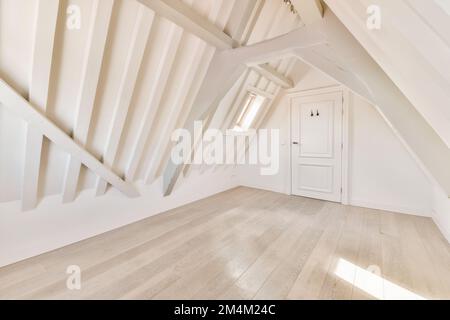 Ein Dachgeschoss-Zimmer mit weißen Wänden und Holzfußboden an der Wand, es gibt eine Tür in der Ecke Stockfoto