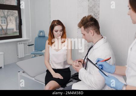 Der Arzt misst den Puls des Patienten während eines Termins in der Klinik, während er auf der Liege sitzt Stockfoto