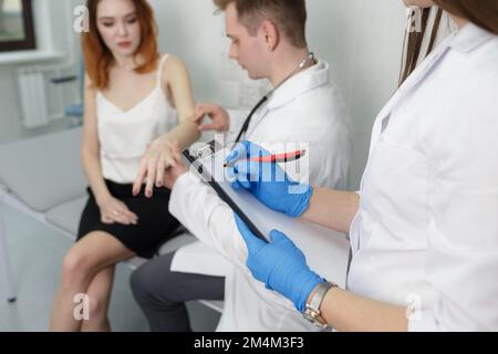 Ein junger Arzt mit einer Krankenschwester, um einen Patienten während eines Kliniktermins zu konsultieren Stockfoto