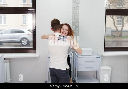 Ein verheiratetes Paar ist glücklich über die Nachricht, dass eine Schwangerschaft ein Bild von einem Ultraschallgerät in der Arztpraxis hält Stockfoto