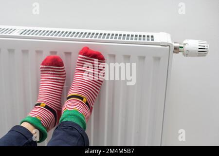 Füße der Person in hellen Wintersocken in der Nähe des Heizkörpers zu Hause Stockfoto