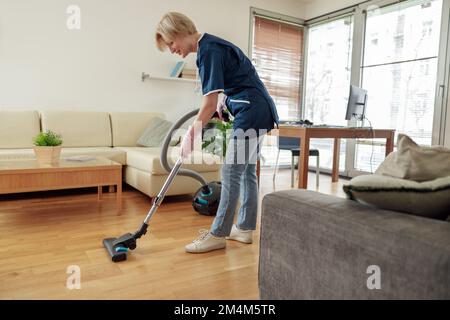 Professionelle Putzfrau trägt Uniform und saugt den Boden im Wohnzimmer Stockfoto