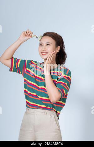 Weibliche Routine-Rollermassage im Gesicht in der Wohnung. Die tägliche Körperpflege hält einen Spiegel Stockfoto