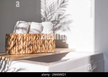 Weiße Badetücher, gerollt in einem Jutekorb auf einem Holzregal, Stauraum im Badezimmer Stockfoto