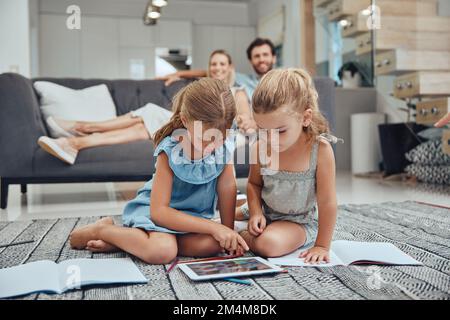Wohnzimmer, entspannte Eltern und Kinder, die e-learning-inhalte auf einem Tablet in Büchern auf dem Fußboden zu Hause machen. Mutter, Vater und Kinder sitzen da Stockfoto