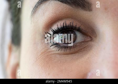 Makro eines braunen Auges eines jungen brünetten Mädchens, Details der Irisblende und der Pupille. Offensichtliche Falten und Krähenfüße als Zeichen des Alters. Stockfoto