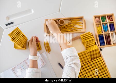 Männliche Kinderhände zählen Mathematik mit goldenen Montessori-Perlen blockieren die Nahaufnahme des Schreibtischs von oben Stockfoto