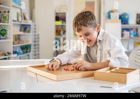 Junge, Kinder, Montessori-Holzbrett mit roten Perlen, Herzform auf dem Schreibtisch Stockfoto